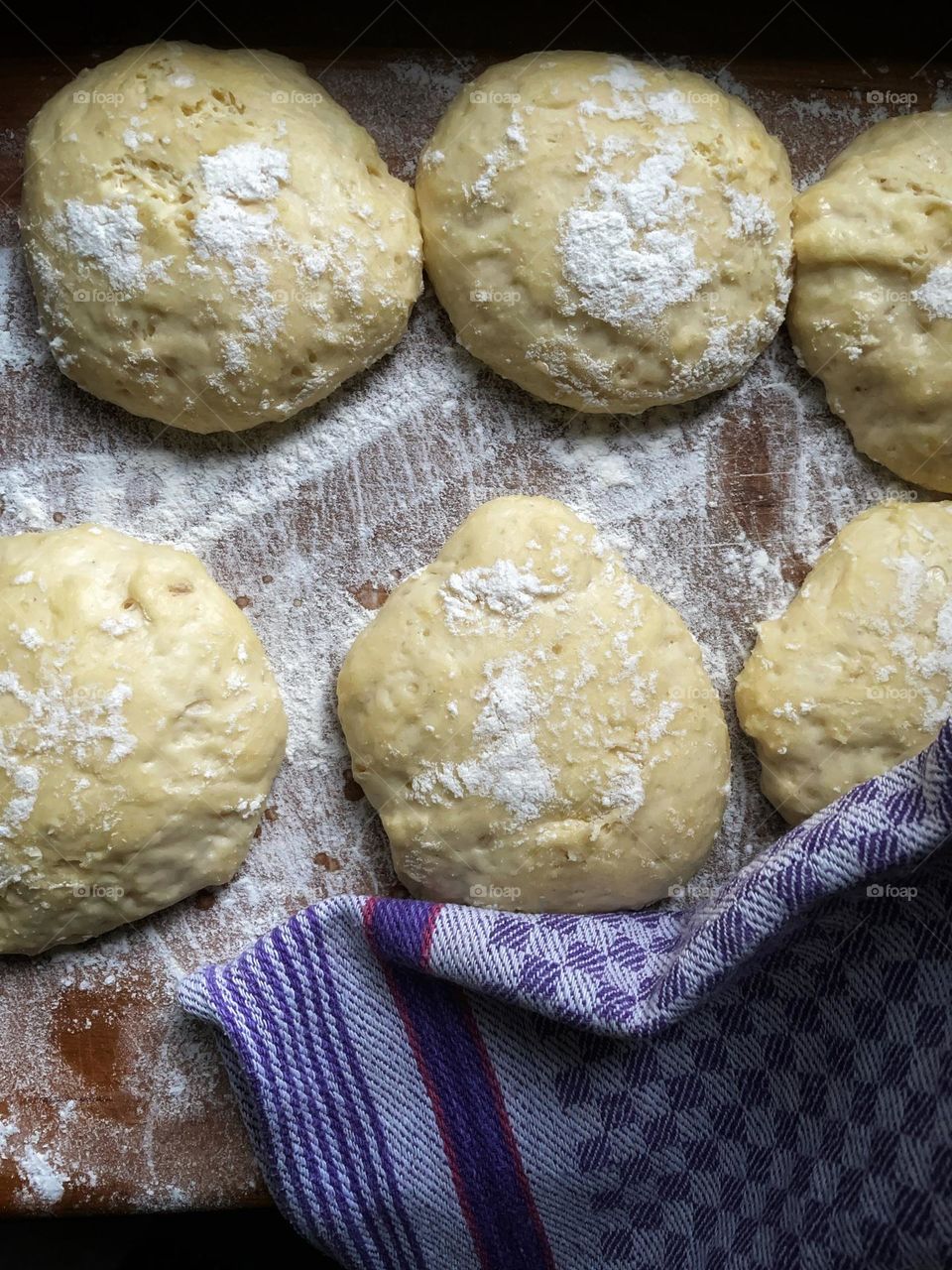 Fresh yeast dough formed into balls lies on a wooden board dusted with flour