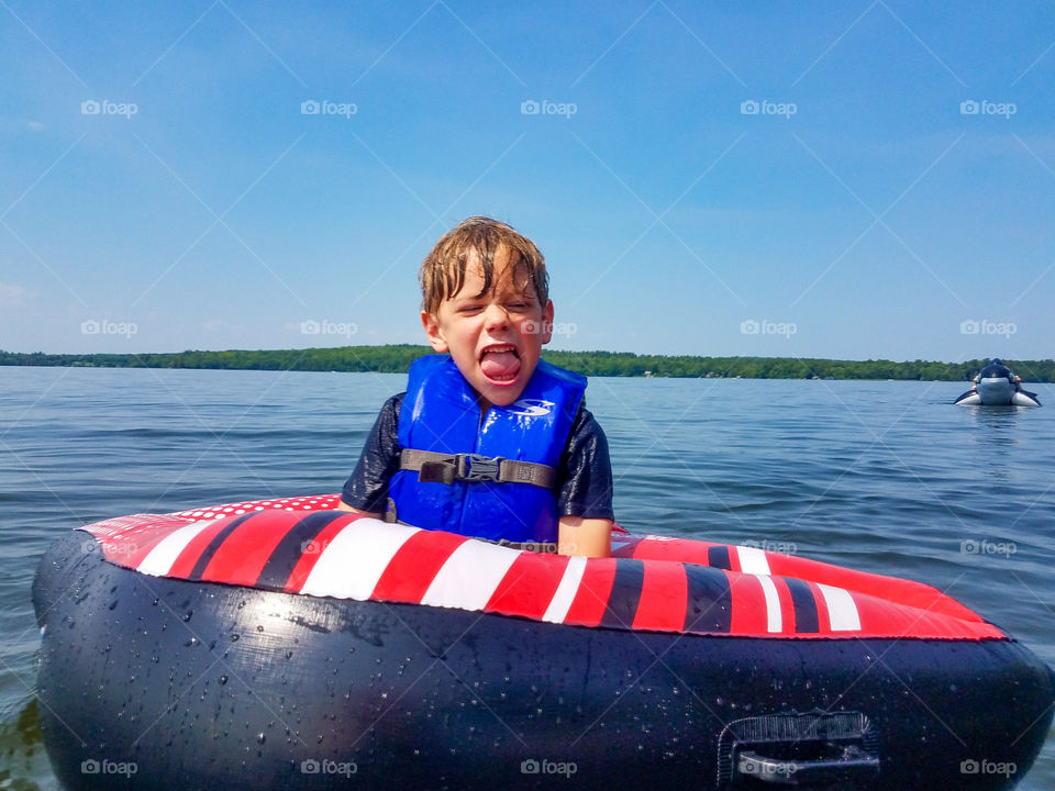 little boy making a funny face in tube on a lake.