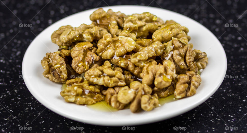 Walnuts with honey on the white plate on the table.