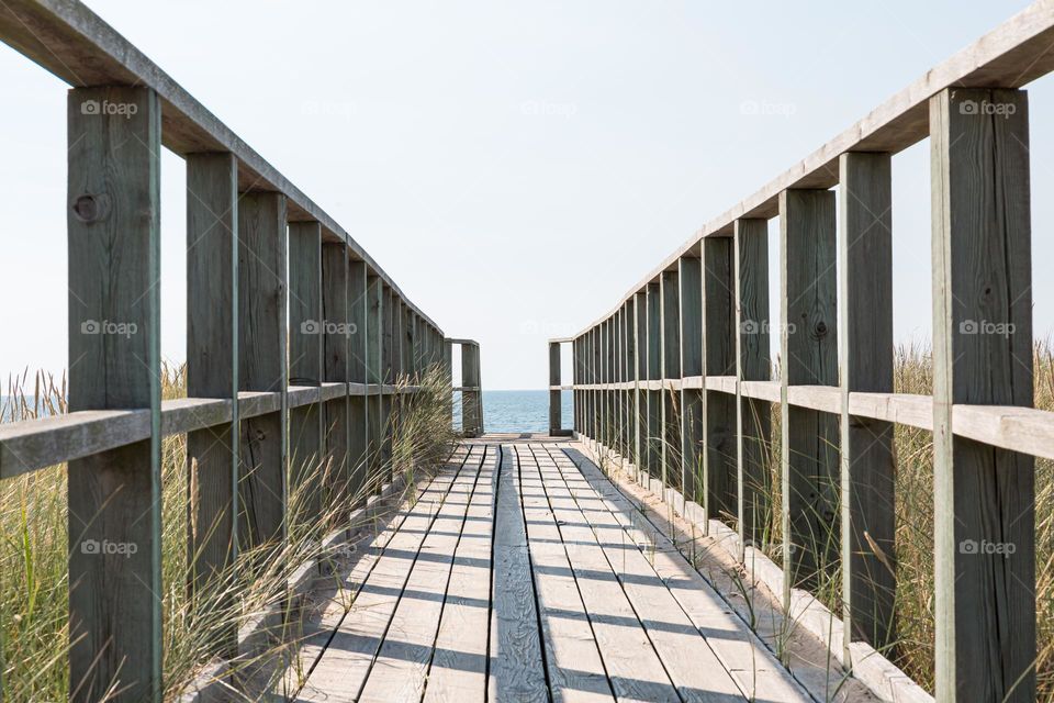 Wooden boardwalk with shadows leading to the ocean and horizon in the distance on a sunny day