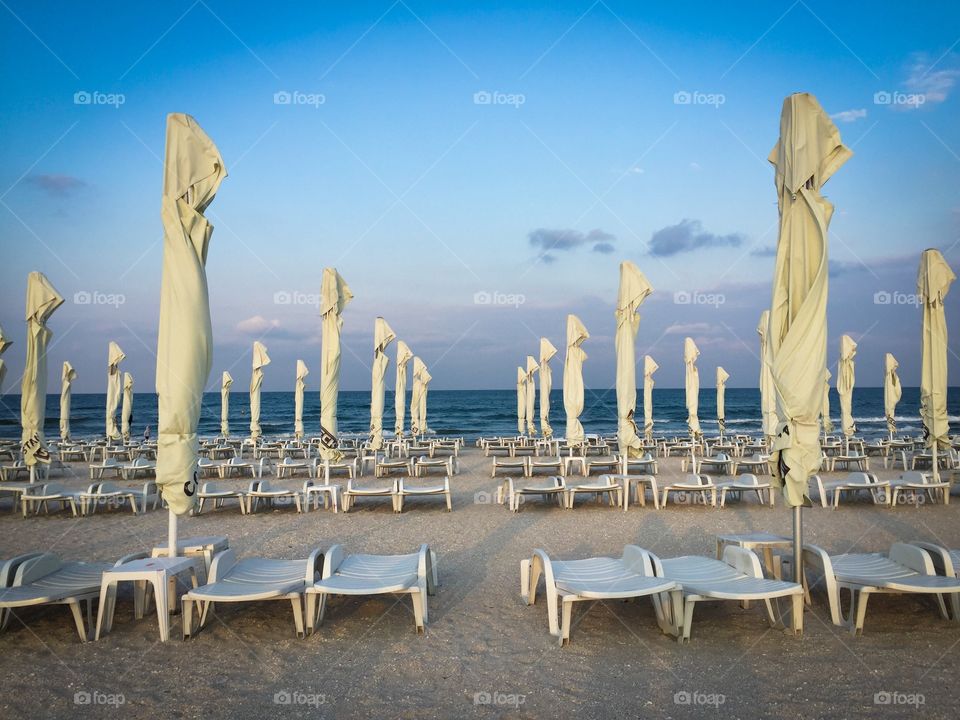 White umbrellas and white sunbeds on an empty beach at dusk