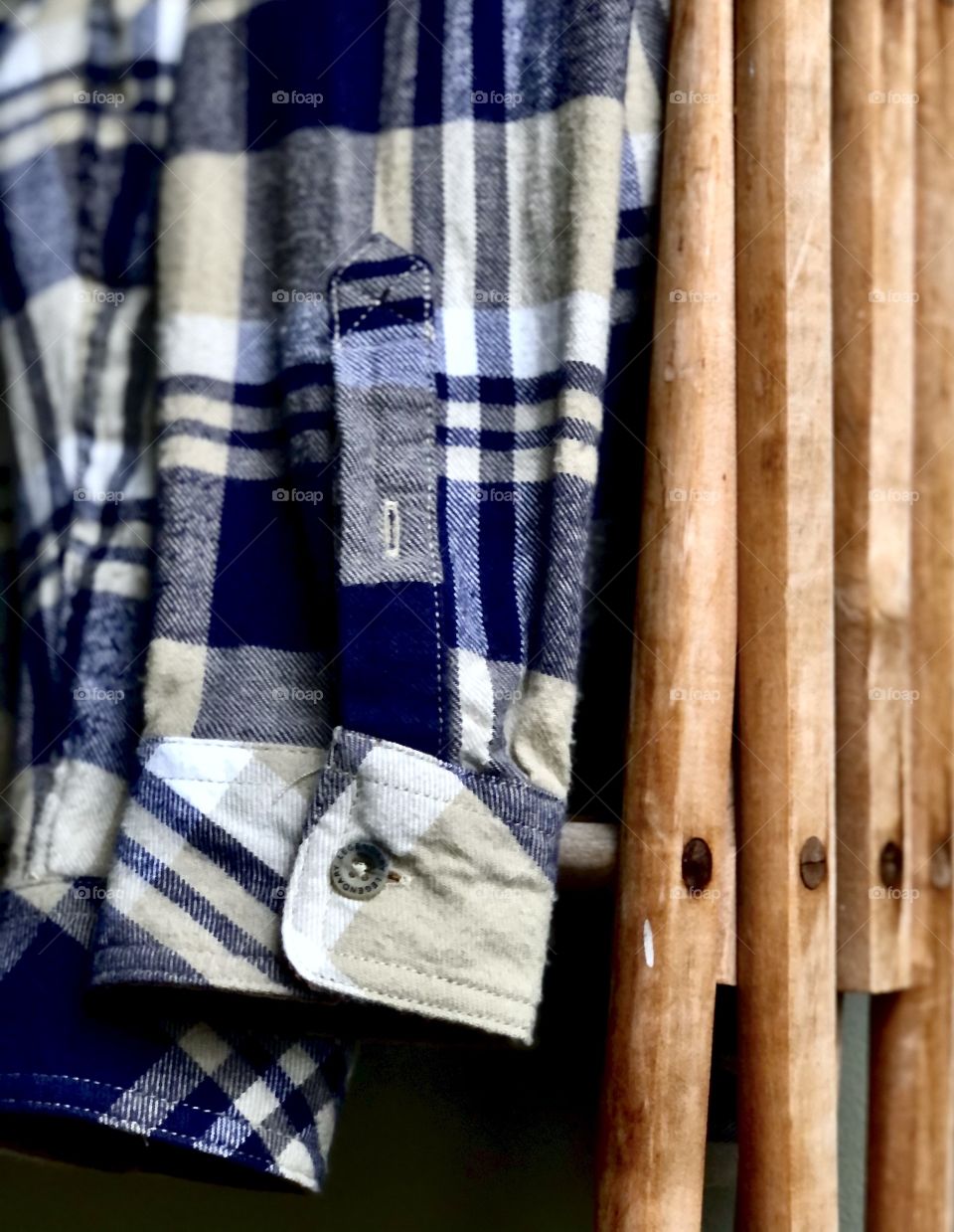 Men’s plaid flannel shirt folded over wooden clothes rack in soft light