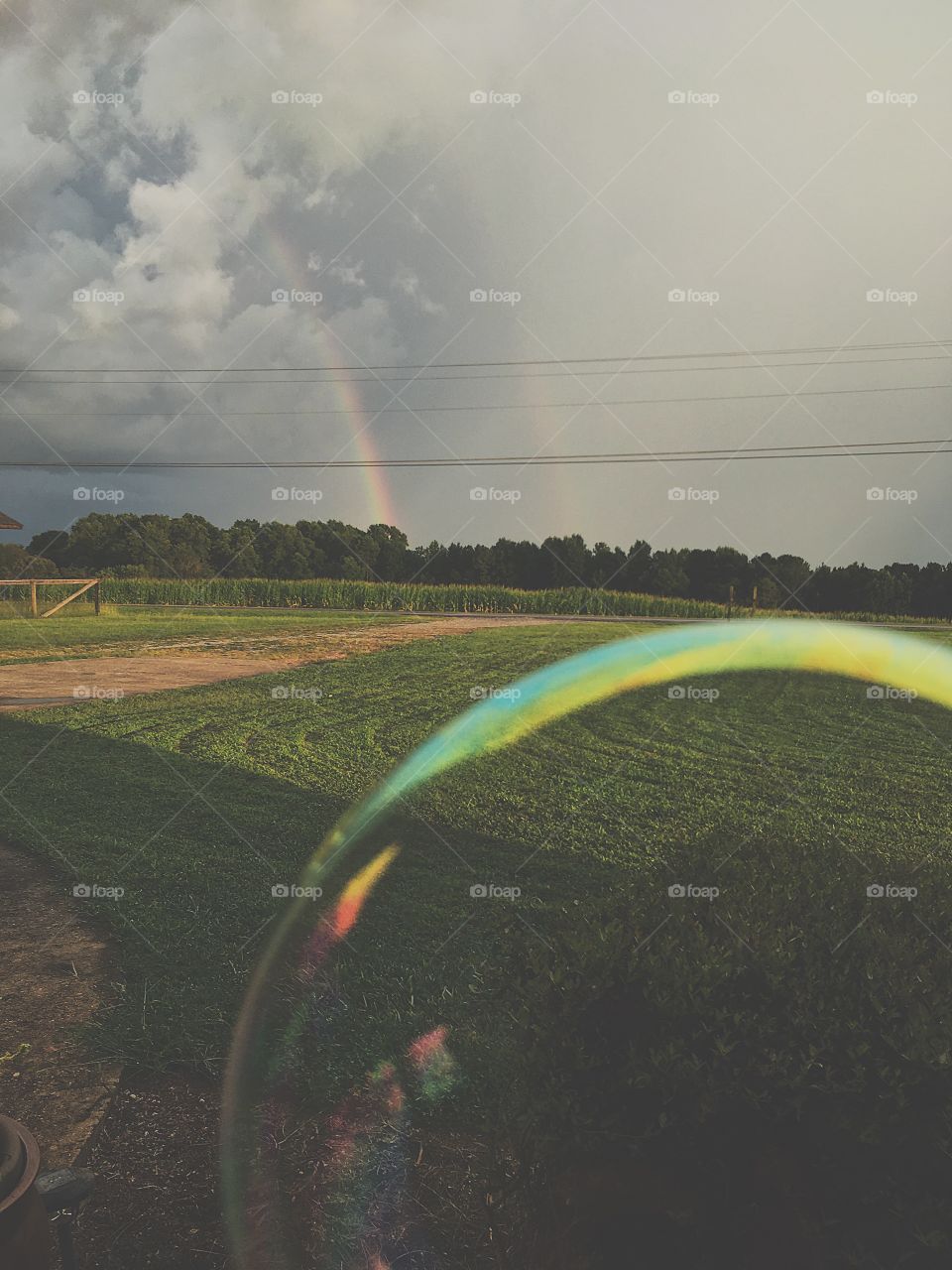 A brightly colored bubble in front of a beautiful green rural landscape with a double rainbow against a stormy sky.