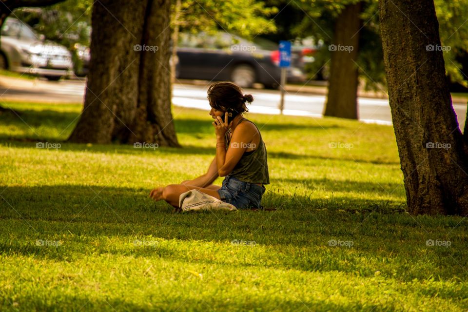 A young woman sitting in the grass making a phone call 