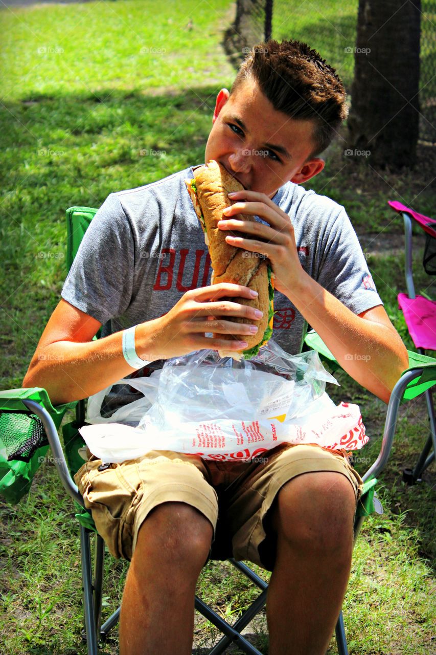 Teenage boy eating burger at outdoors
