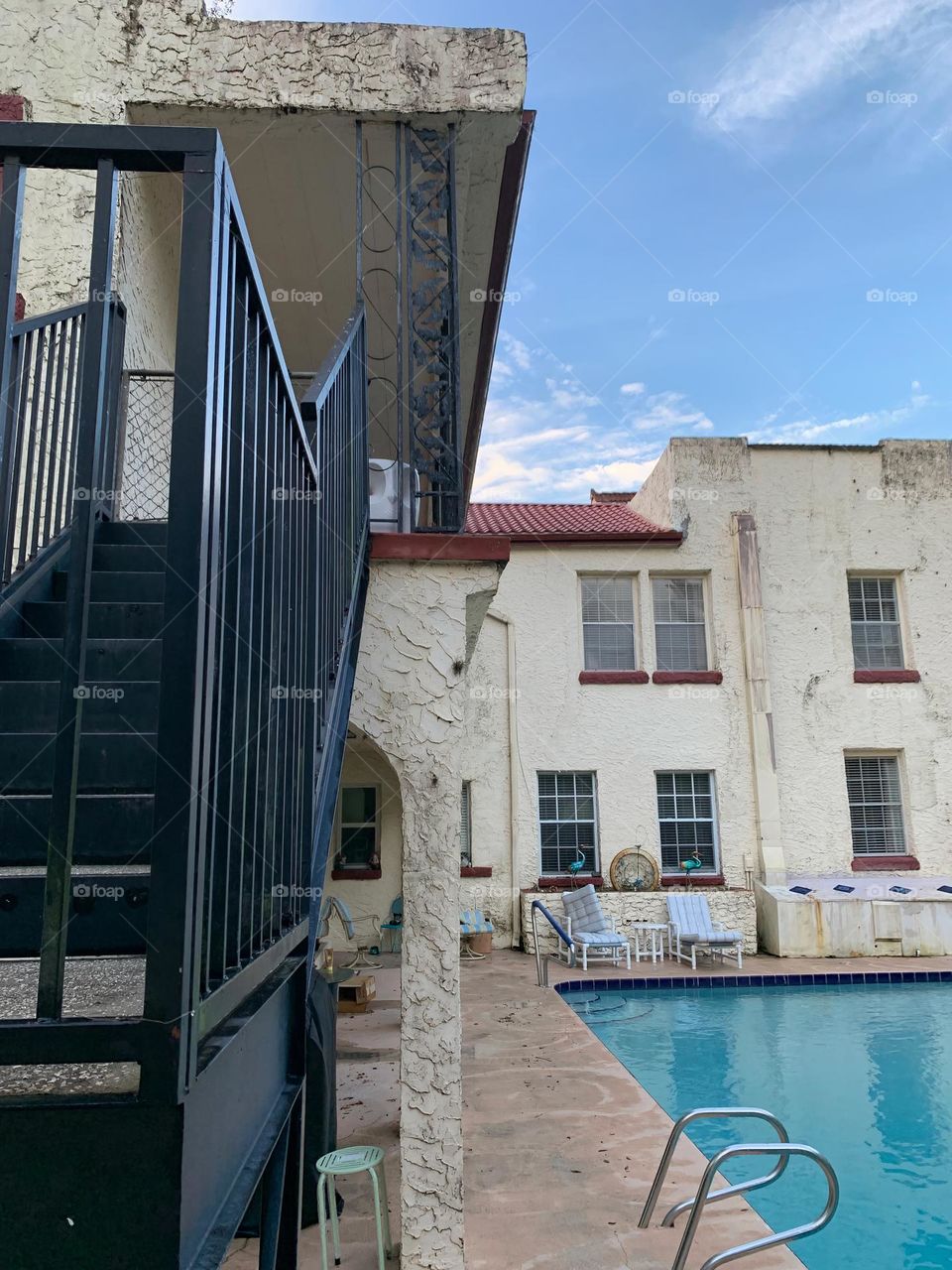 White and red spanish old style architecture residential large house built in the early 1900s. Many windows on the side of the house low angle with aging signs with charming pretty style and beautiful landscaping with pool and chairs with a staircase