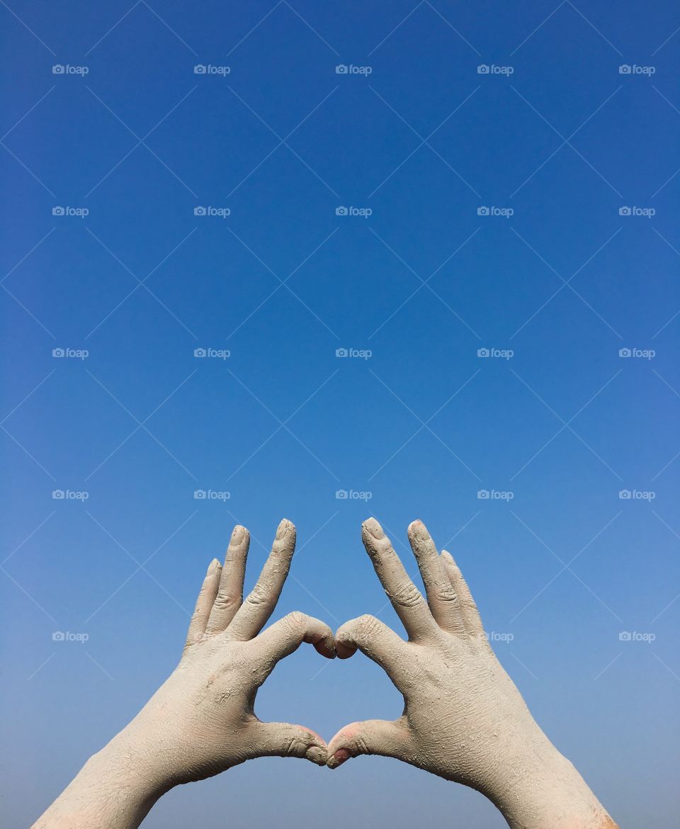 two human hands against the clear blue sky, the fingers indicate a heart shape