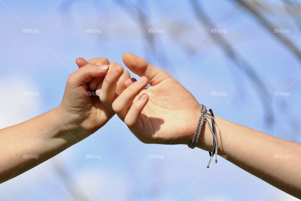 Two girls hands holding together on blue sky background 