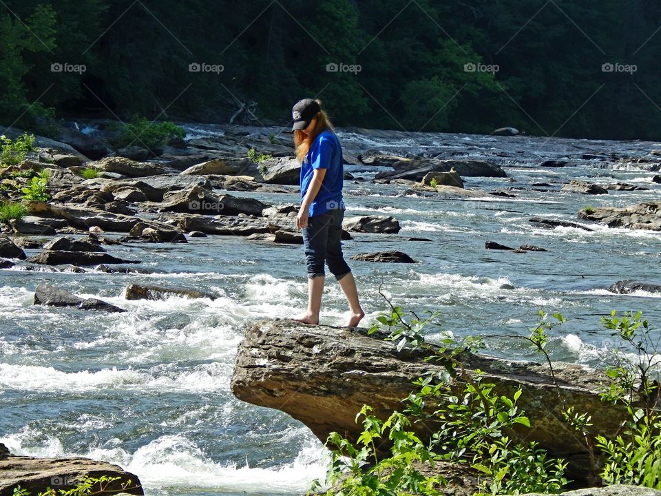 yound girl standing on large boulder extending over the Chattooga river