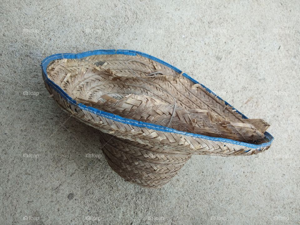 The old and broken weaved bamboo hat that used for a long time is on the concrete floor.