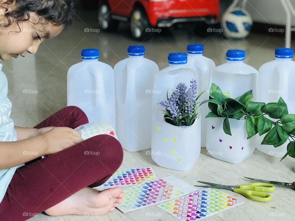 Girl making flower pots from leftover milk bottles.