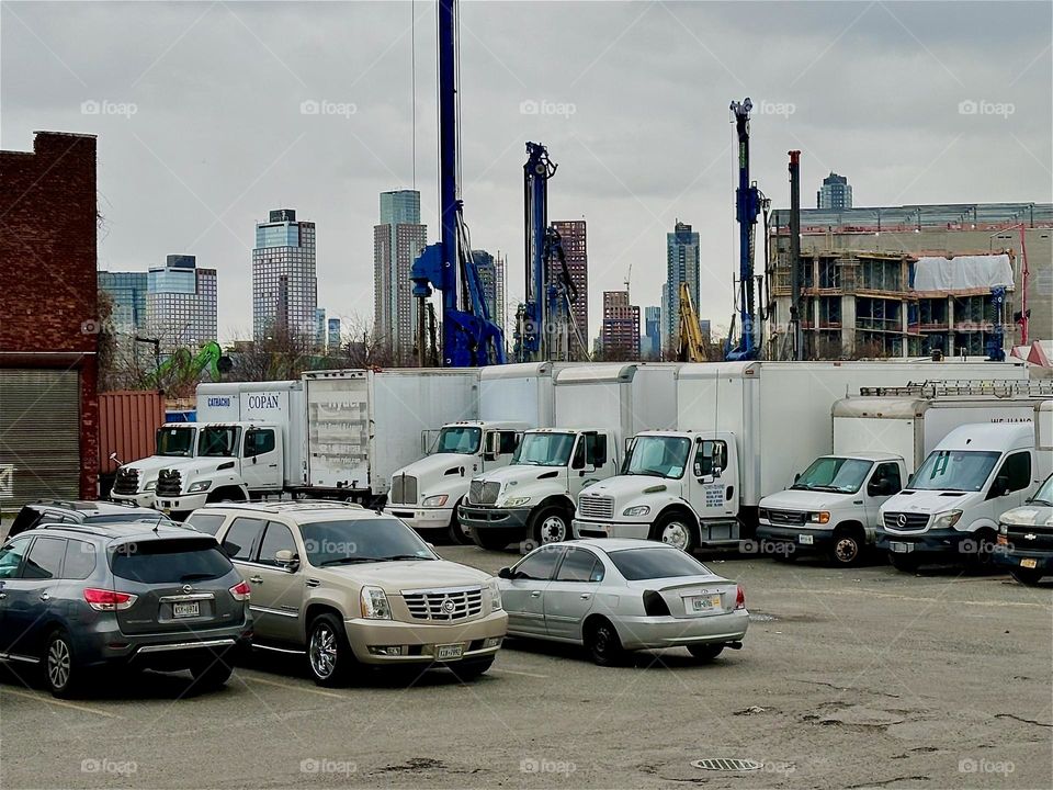 This is the parking lot of „ACCESS Storage“ on „Review Avenue“ near „Borden Avenue“, the BQE and „Dutch Kills“. Company trucks are parked here ready to go out. The „Manhattan“ skyline can be seen in the distance. 2023. Hypnotic Productions
