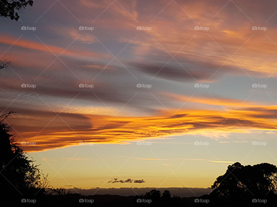 Summer time in NZ. A beautiful sunset again taken from the view at my house. Notice the dark clouds blending with the bright.Gentle rain clouds sitting in front of the colorful clouds. Thank you universe❤