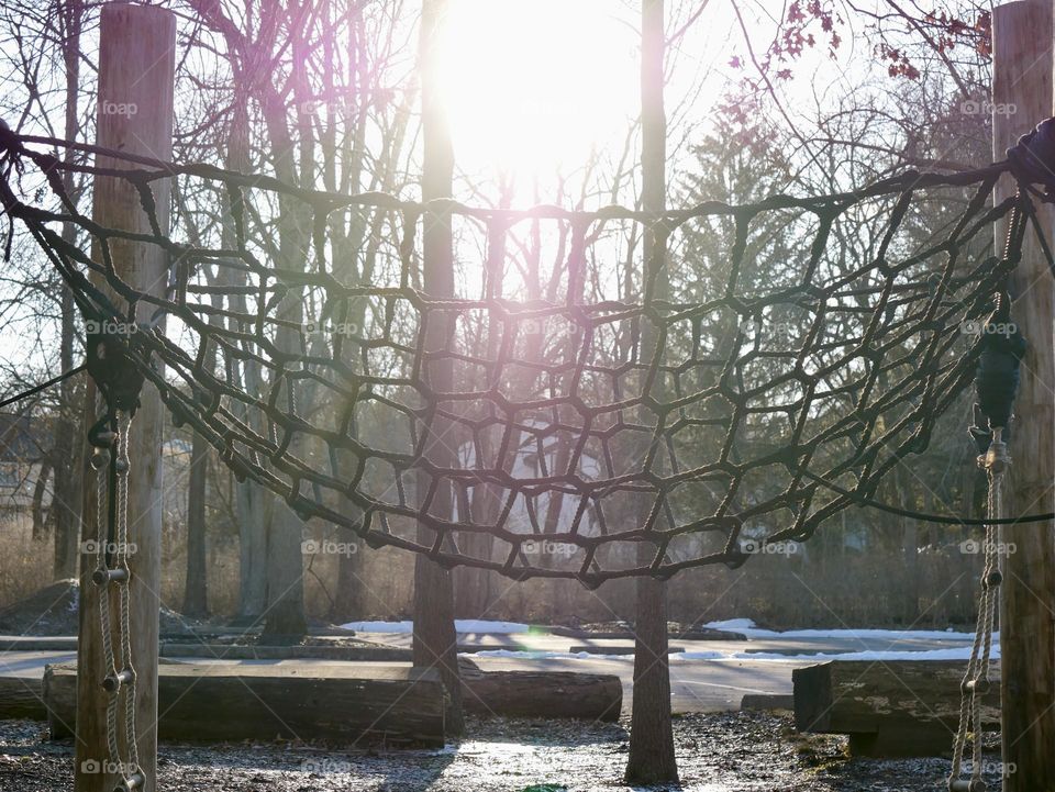 A web of rope on a children’s playground, with the sun and trees in the background. 