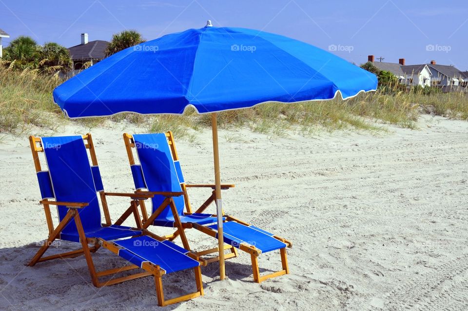 Two blue beach chairs and umbrella at the seashore. 