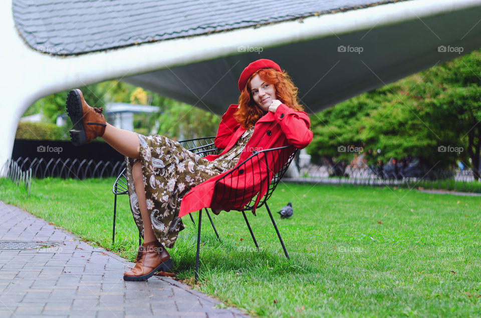 Portrait of a young redhead curly woman in red coat with freckles and blue eyes walking in autumn park. Happy people.