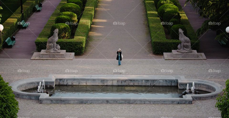 Girl taking a photo in the park near a water fountain