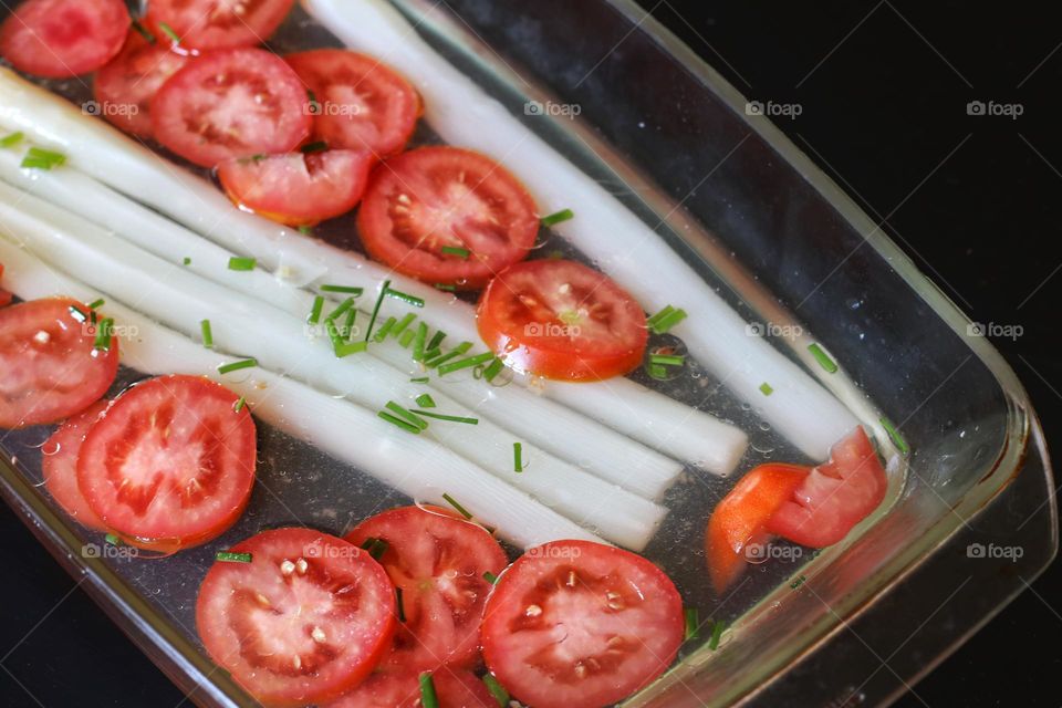 Tomato salad and asparagus with chives in a glass bowl on black table 