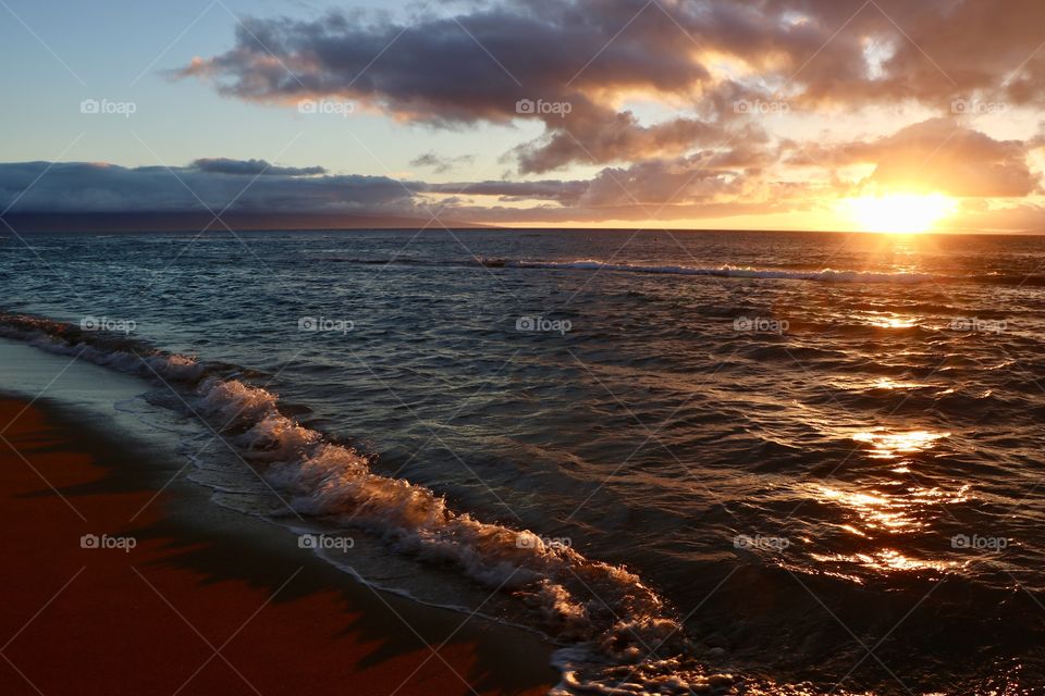 Sunset on a tropical beach , clouds making the scenery dramatic and golden light casted on the beach giving a very warm feeling for the viewers..