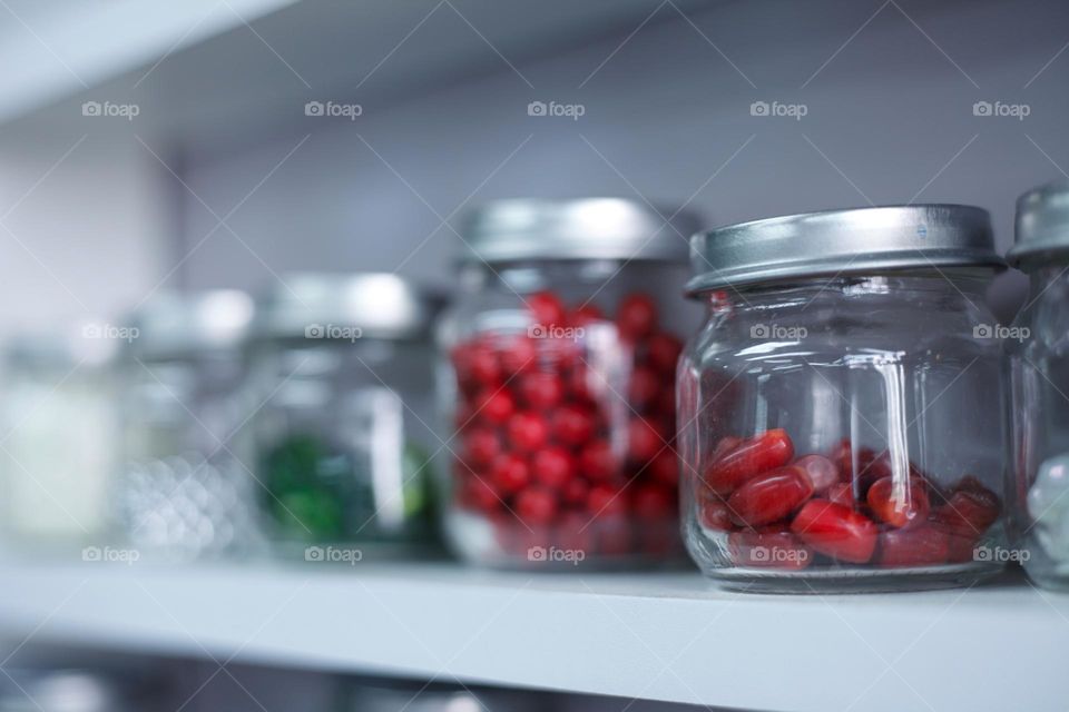 red candy pills or multi-colored beads on a shelf in jars