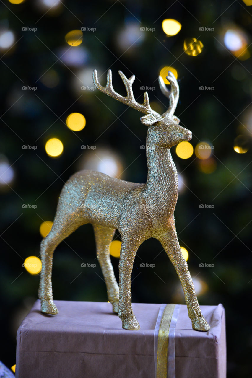 новогодняя золотая игрушка оленя на фоне огней елки