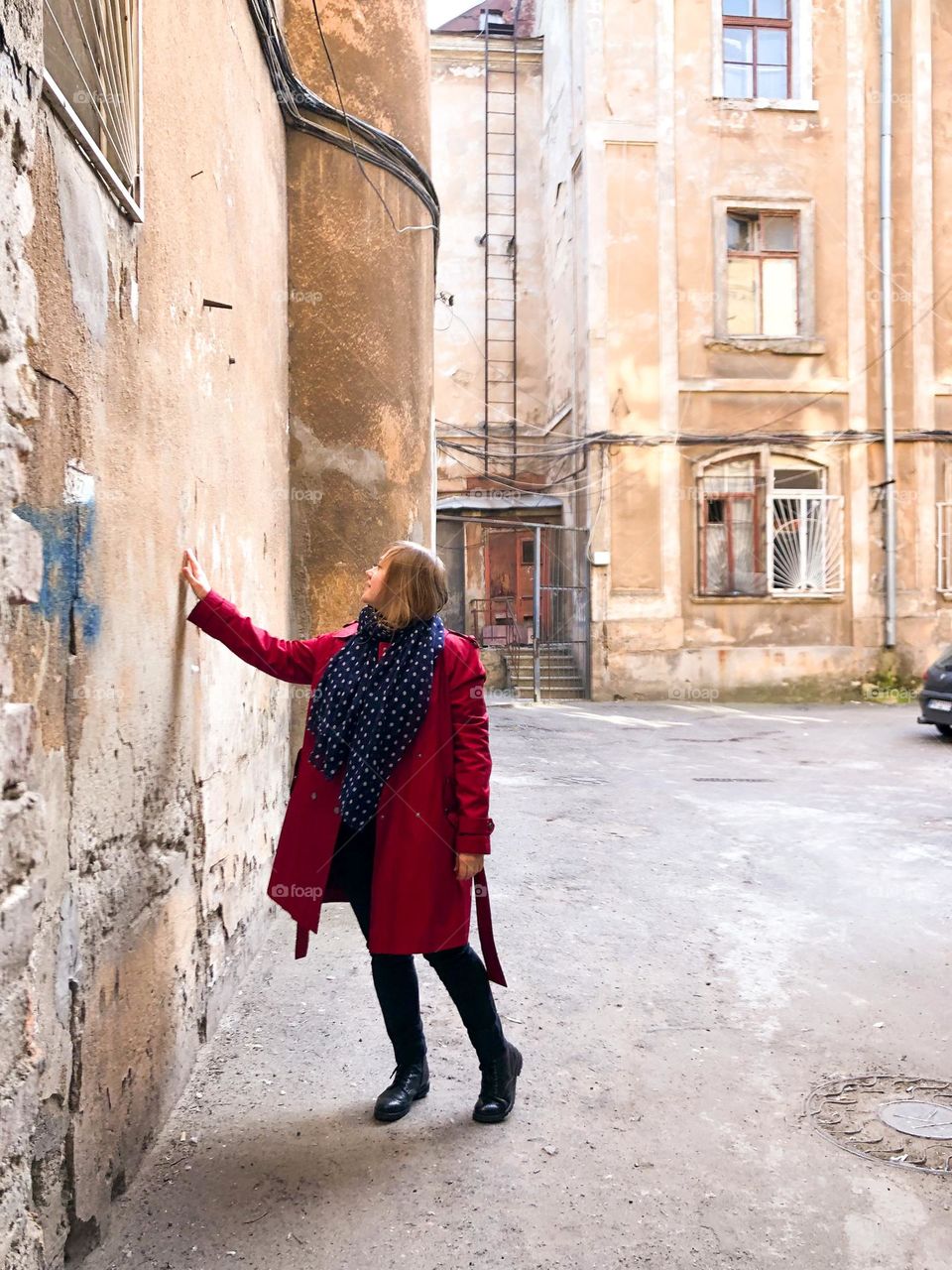 Woman in a red trench coat in the yard of the old building 