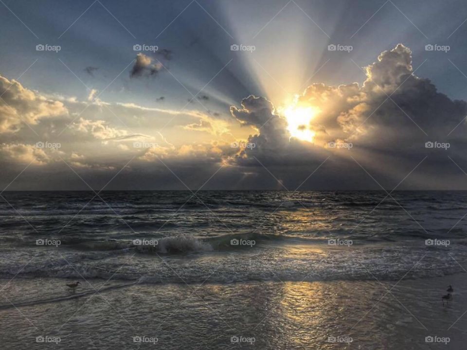 Serene sunset behind the clouds at the beach with waves coming to shore