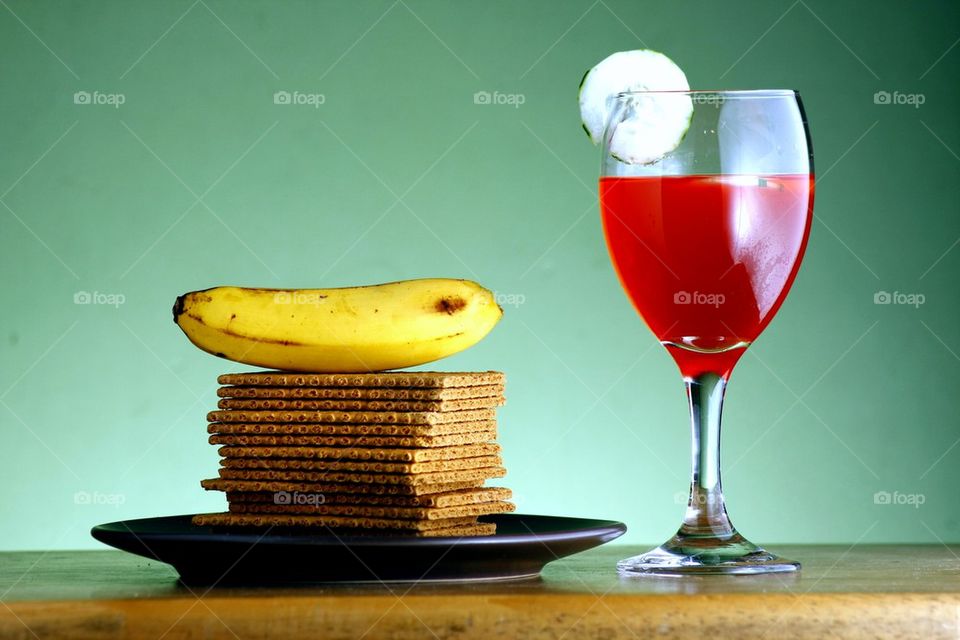 stack or pile of soda crackers, a banana and a goblet of fruit juice with cucumber slices