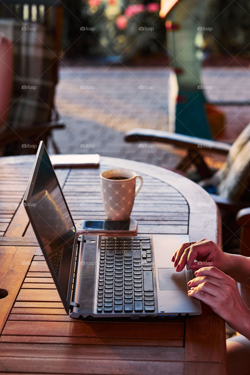 Woman working at home, using portable computer, sitting on patio on summer day. Candid people, real moments, authentic situations