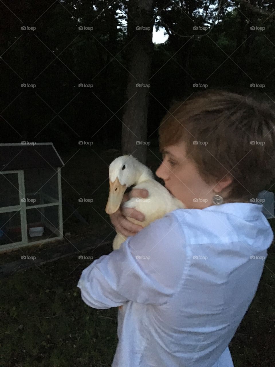 A pretty, formally-dressed, young woman holds her pet duck in her arms on a dark evening