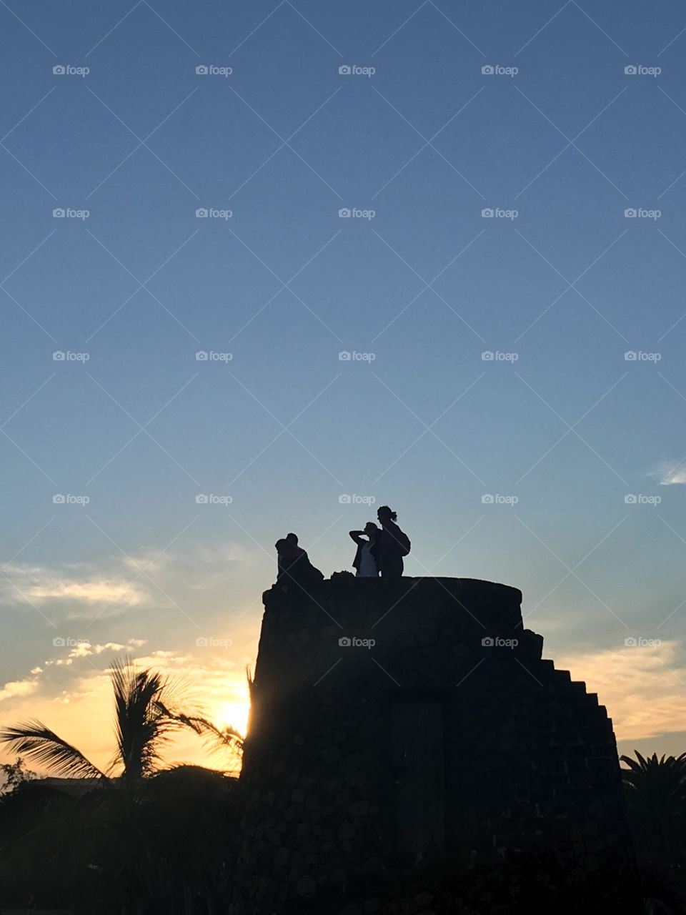 The sun setting behind an ancient tower in the coastal town of Costa Teguise on the island of Lanzarote. Tourists can be seen admiring the last few minutes of sunlight from atop the stone tower.