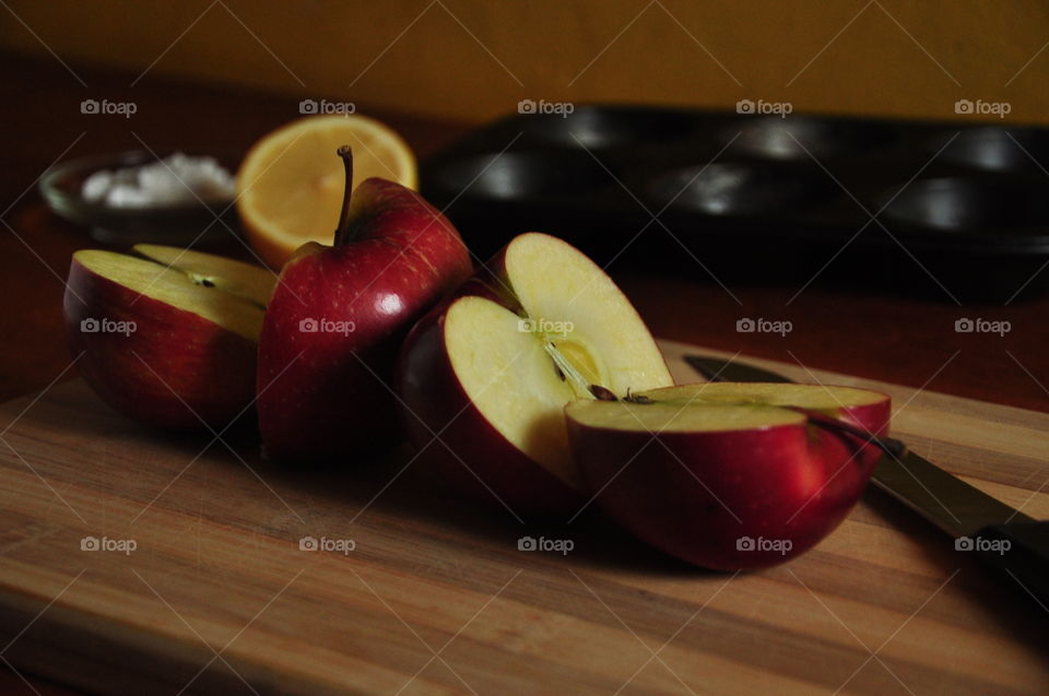 red apples cut in half with lemon muffin baking utensil and flour on wooden kitchen board
