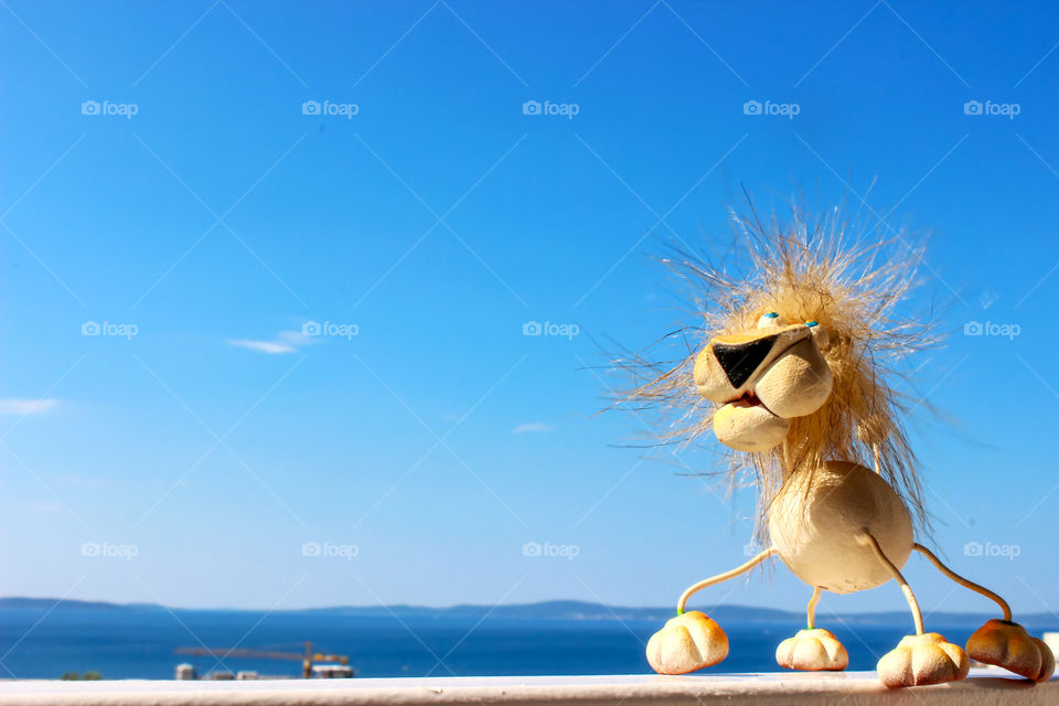 Blue sky and sea behind the lion toy on a balcony fence