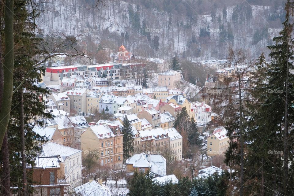 A View from above to snowy Karlovy Vary city through fir branches
