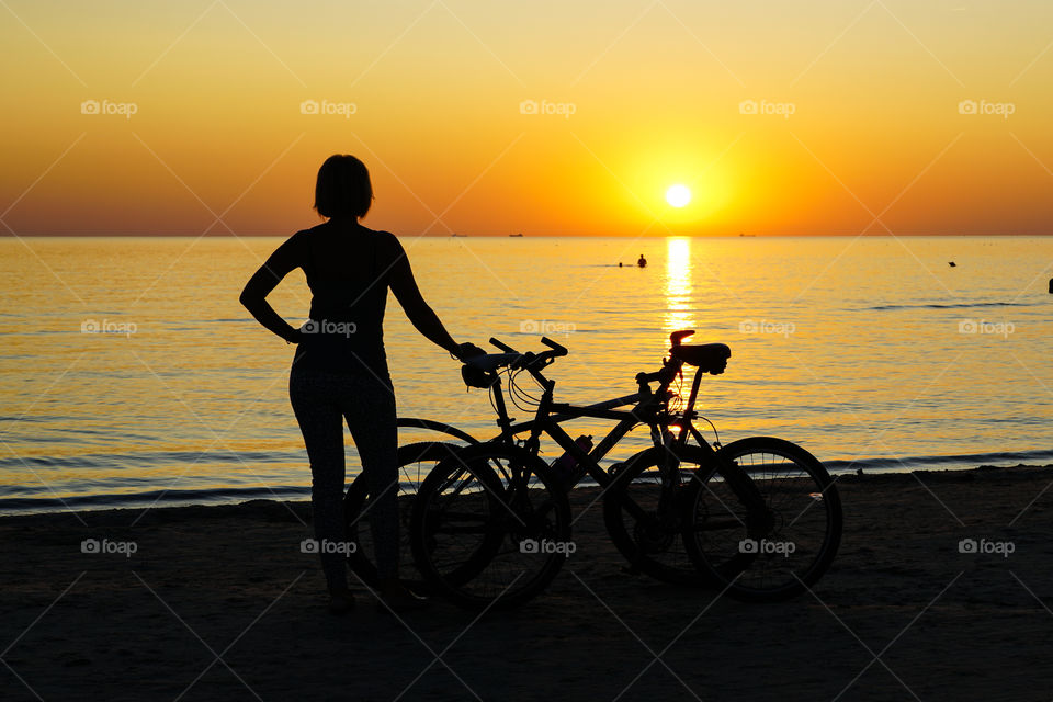 woman silhouette with bike at sunset by the sea