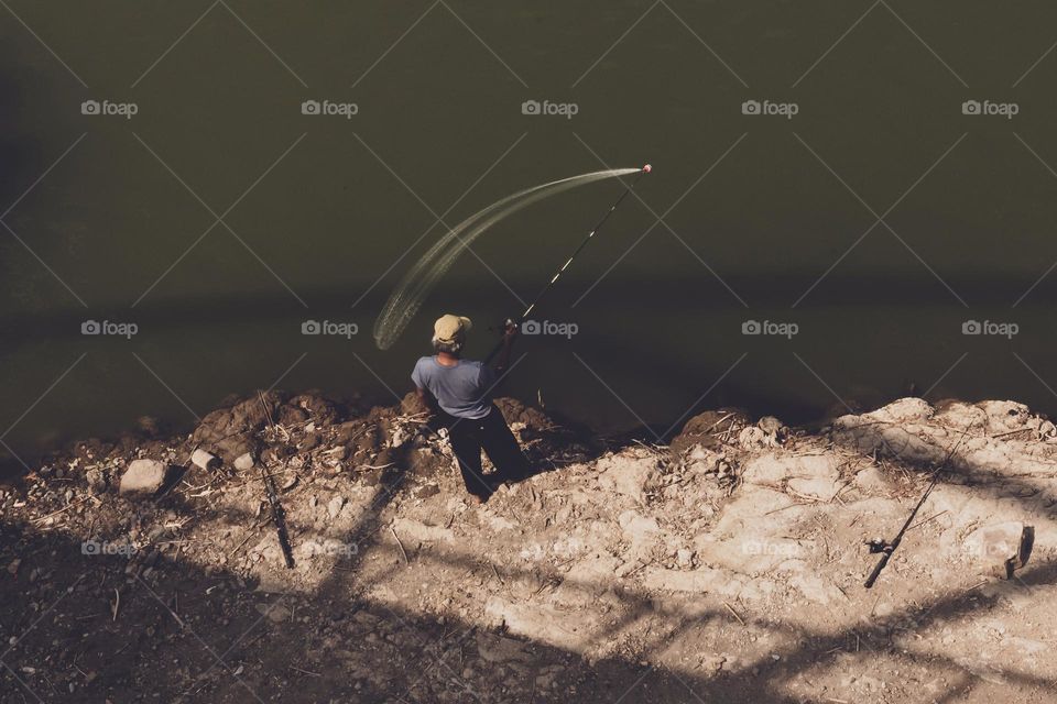 a man under the bridge, enjoy his fishing activity alone by the lake during daytime