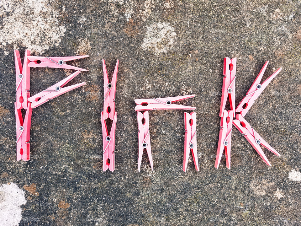 The word Pink spelt out with bright pink clothes pegs on a stone background.