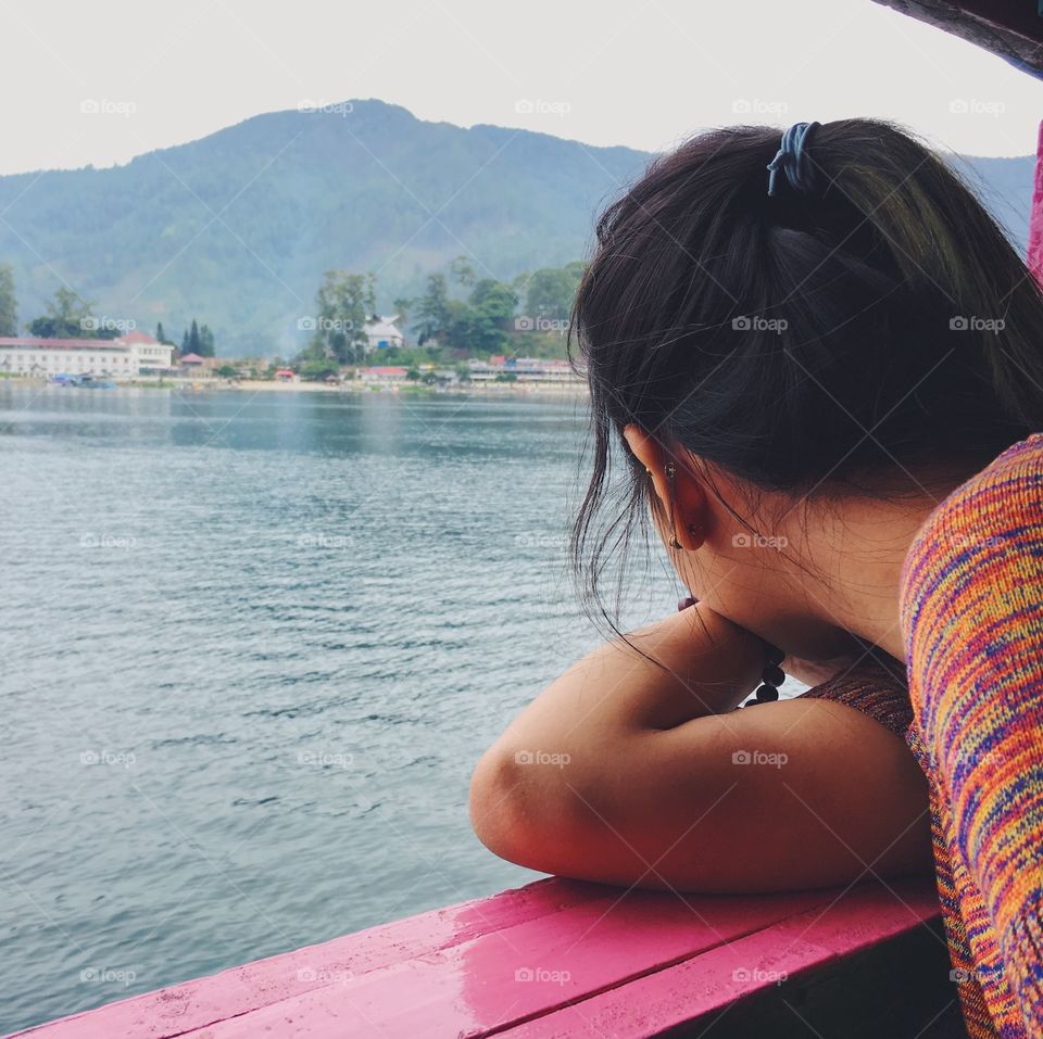 A girl with her back facing the camera looks at an island in the distance while on a boat on Lake Toba in Medan, Indonesia.