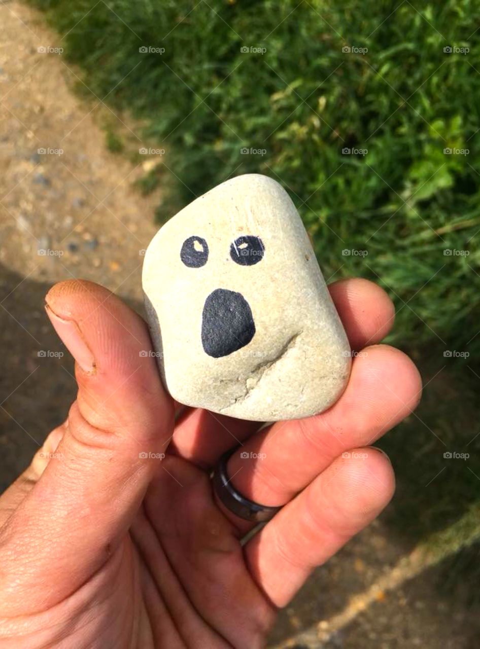 Funny humorous face painted on a small rock in the countryside held in hand