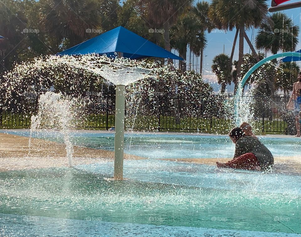 Children having lots of fun in the water at the colorful kids splash pad at the city park for children during a really warm day in Florida.