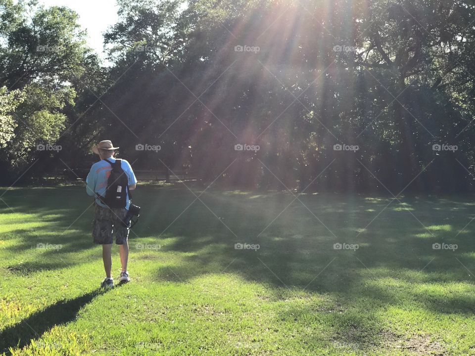 Man hiking through the woodland bathed in rainbow sun rays.