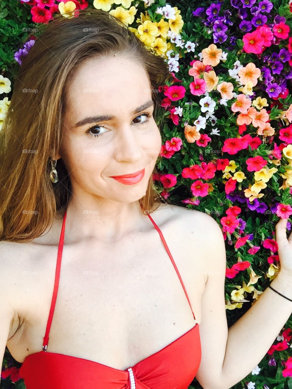 Portrait of woman with dark blonde hair and black eyes with wall of flowers in the background