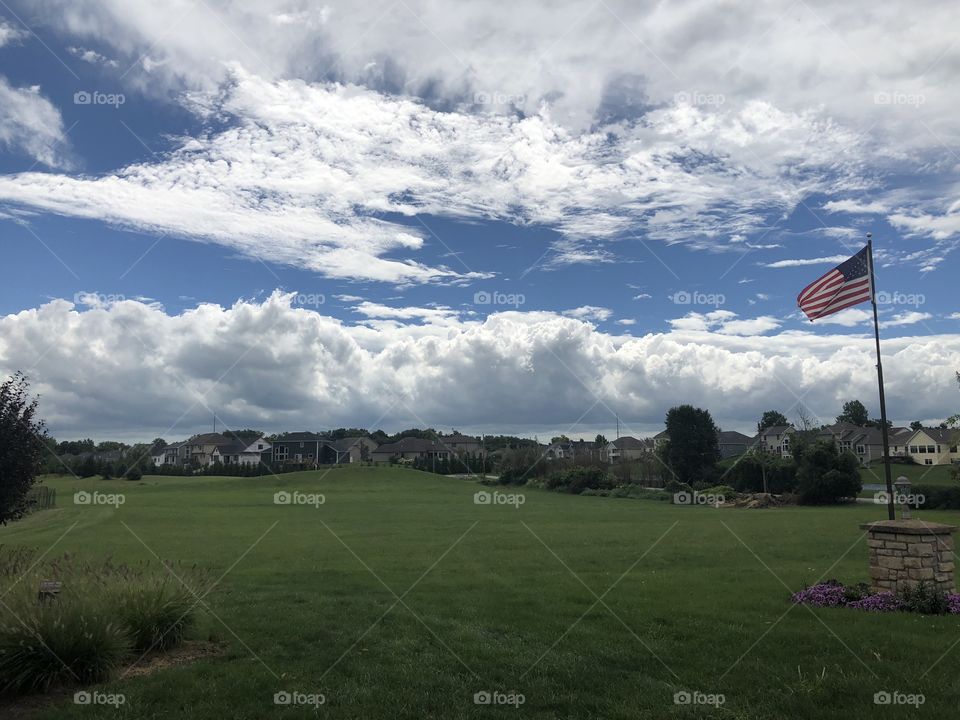 View of field and sky with clouds. American flag to the right.