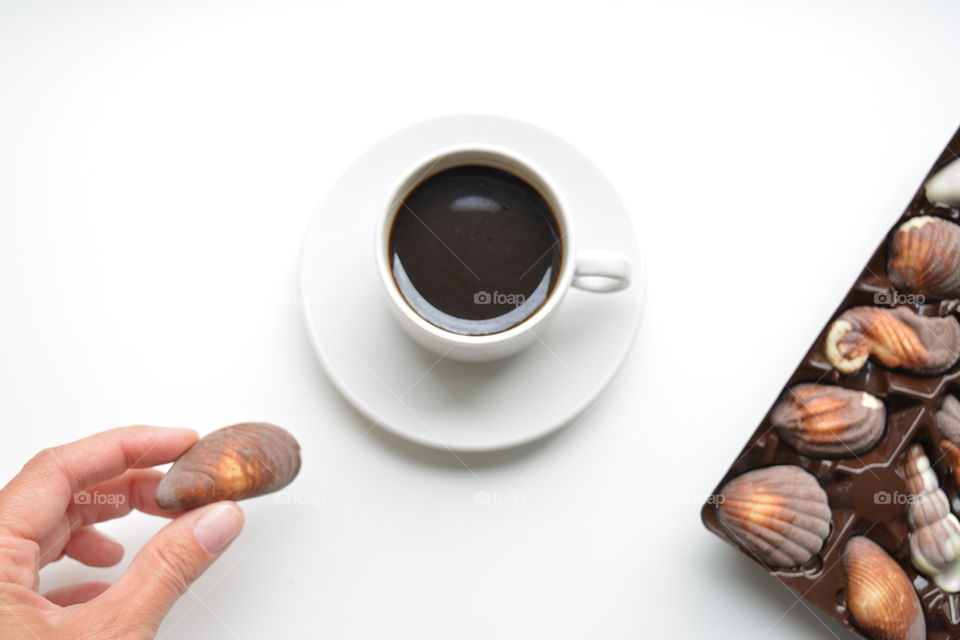 coffee mug and chocolate candies on a white background top view, female hand with candy