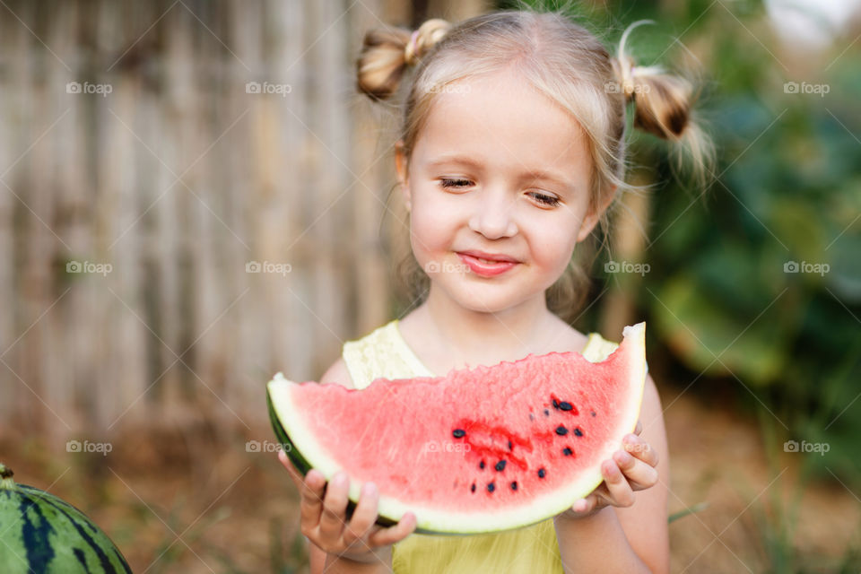Little girl with blonde hair holding fresh watermelon 