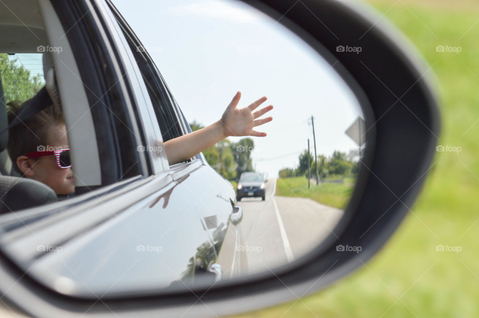 View from the reflection in a side view mirror of a young boy with his hand sticking out of a car window