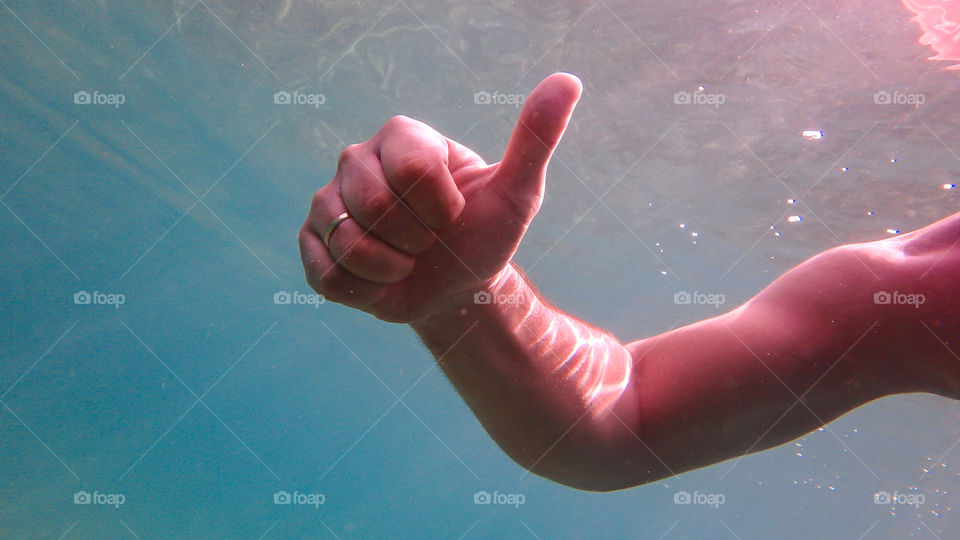 Man diving in the ocean, male underwater smiling,swimming and relaxing in big blue sea with his waterproof camera and thumb up