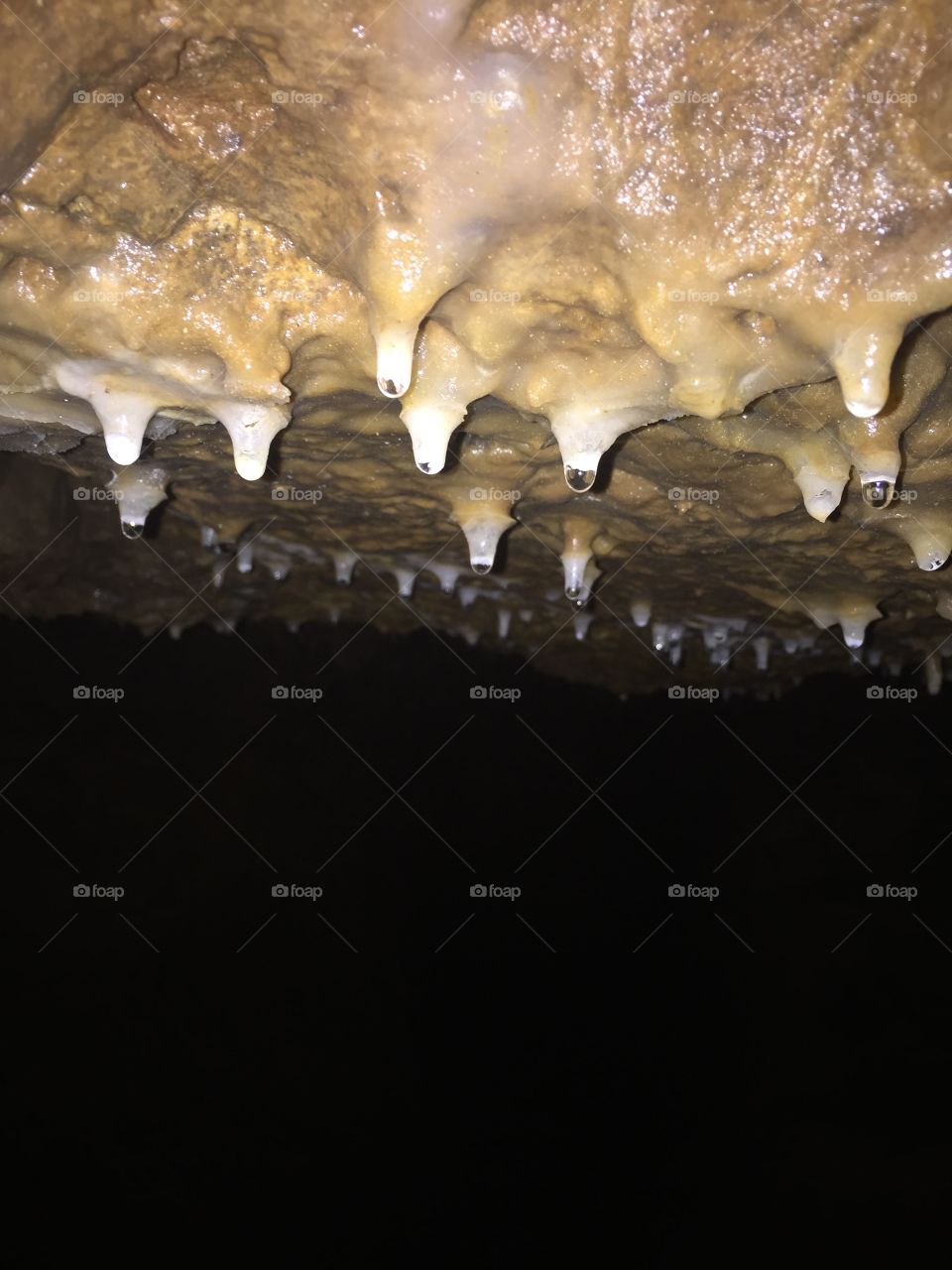 Drops of water hanging off of small stalactites beautifully highlighted by the pitch black background