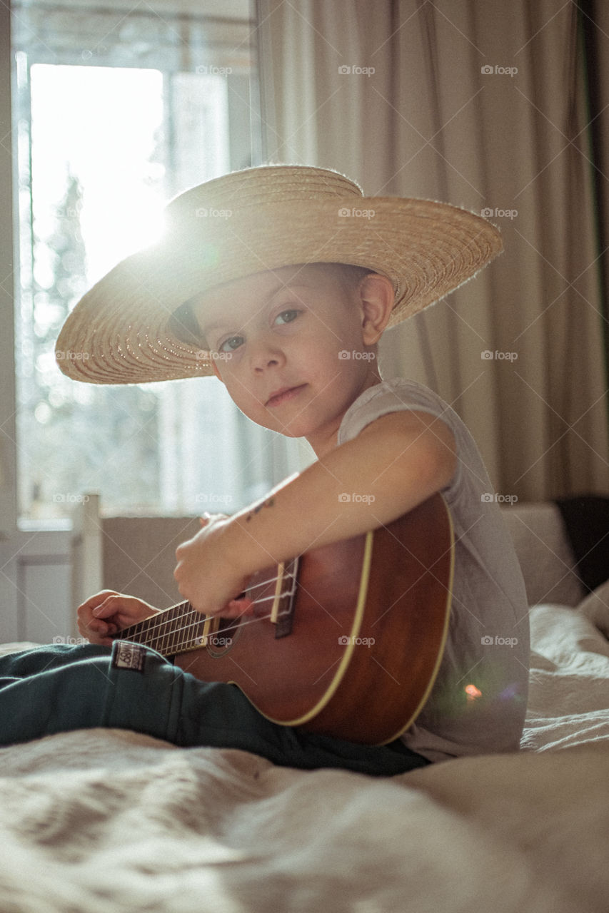 Little boy playing ukulele guitar in hat