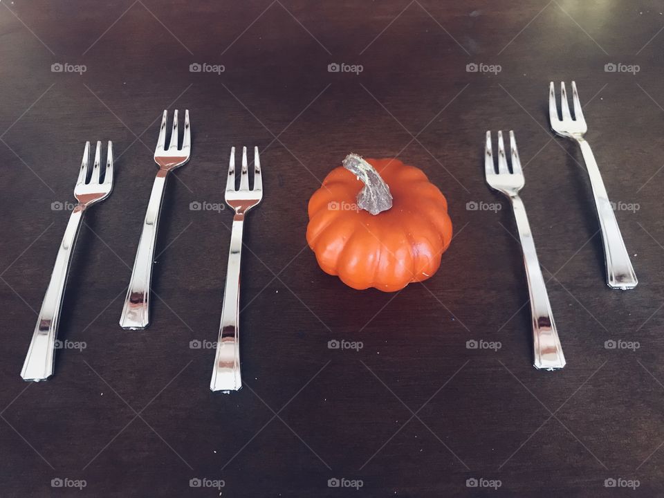 A beautiful table display of a mini orange pumpkin on the dark wooden table top surrounded by mini silver forks 